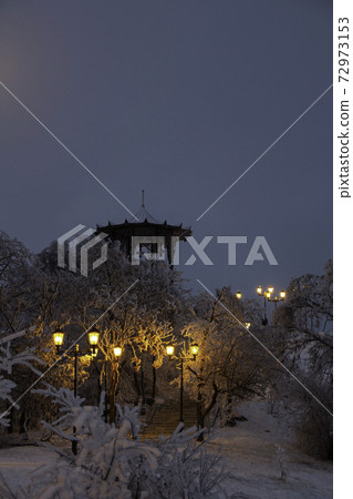 Winter evening view of the park. Ladder in the snow. Chinese gazebo in Pyatigorsk. Lantern light illuminates the road. Background for calendar, postcards. Winter evening view of the park. Ladder in the snow. Chinese gazebo in Pyatigorsk. Lantern light illuminates the road. Background for calendar, postcards. 72973153
