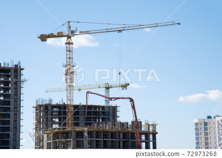 Tower crane lifting a concrete bucket at construction site. Tower crane lifting a concrete bucket at construction site. 72973268