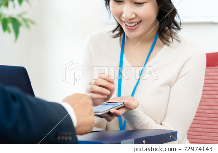 A woman having a meeting while looking at her smartphone 72974143