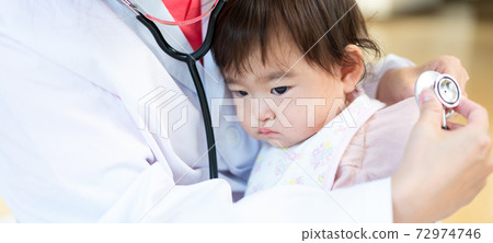 Young female doctor embraced and examined by a sleepy-faced baby banner size Young female doctor embraced and examined by a sleepy-faced baby banner size 72974746