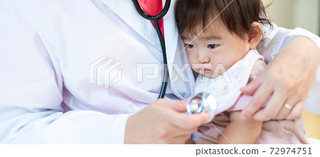 Young female doctor embraced and examined by a sleepy-faced baby banner size 72974751