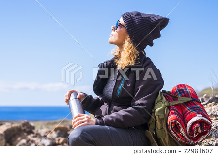 Active caucasian woman resting sit down after a trekking walk -outdor leisure acitivity for healthy people -ocean. view and blue sky in background -sunny day of summer Active caucasian woman resting sit down after a trekking walk -outdor leisure acitivity for healthy people -ocean. view and blue sky in background -sunny day of summer 72981607
