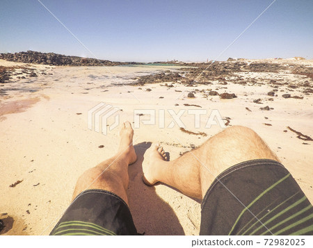 Summer vacation at the beach concept with alternative point of view of man legs and sand - relax and enjoy the ocean outdoor for people 72982025