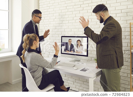 Team of business people video calling colleagues for work meeting and waving hands at screen 72984823