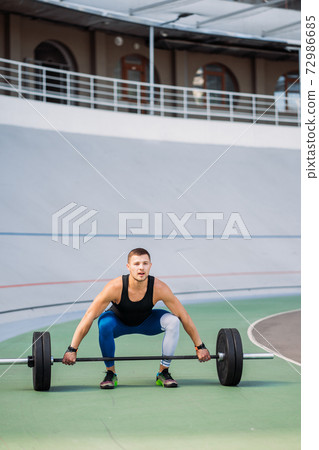 Young guy raises the bar in the stadium, outdoor workout 72986685