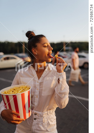 Young cute woman holding popcorn in a shopping mall parking lot Young cute woman holding popcorn in a shopping mall parking lot 72986734