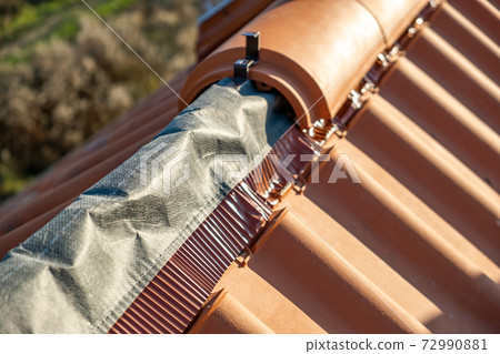 Closeup of yellow ceramic roofing ridge tiles on top of residential building roof under construction. 72990881