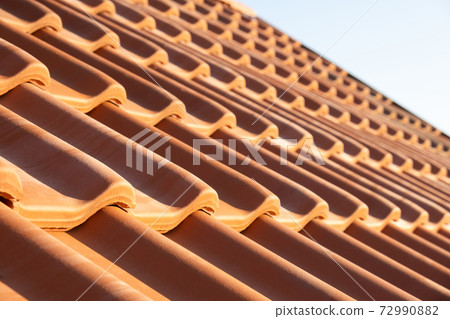 Overlapping rows of yellow ceramic roofing tiles covering residential building roof. 72990882