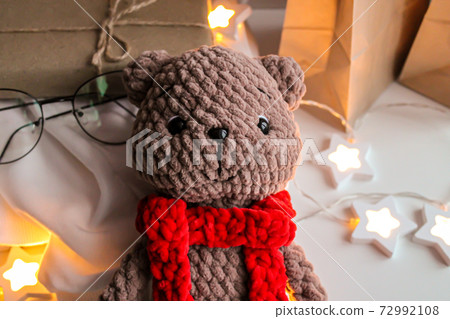 Brown knitted teddy bear with a red scarf lies on the table Brown knitted teddy bear with a red scarf lies on the table 72992108