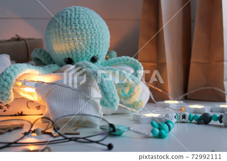 Blue knitted octopus toy sits on a white sweater on the table Blue knitted octopus toy sits on a white sweater on the table 72992111