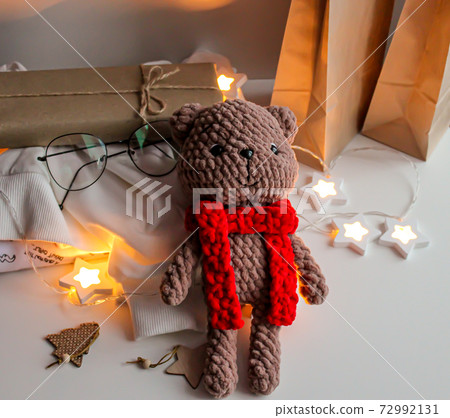 Brown knitted teddy bear with a red scarf lies on the table Brown knitted teddy bear with a red scarf lies on the table 72992131