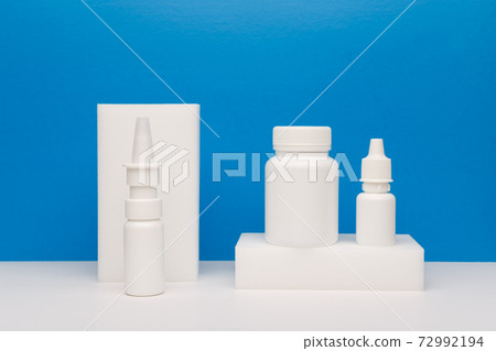 Medical still life with nose spay, eye drops and pills on white podium against blue background 72992194