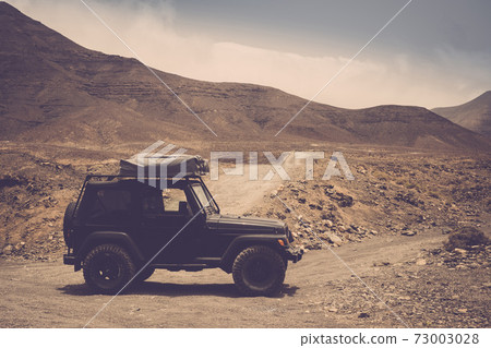 Black off road car vehicle in the desert with mountain and roads in background - concept of alternative way of travel and live in adventure lifestyle for alternative people Black off road car vehicle in the desert with mountain and roads in background - concept of alternative way of travel and live in adventure lifestyle for alternative people 73003028