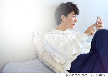 Young man touching a smartphone on the bed Young man touching a smartphone on the bed 73003057