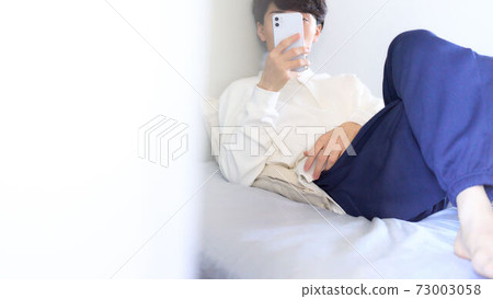 Young man touching a smartphone on the bed Young man touching a smartphone on the bed 73003058