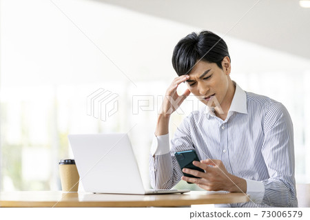 A young man holding his head while looking at the screen of a smartphone A young man holding his head while looking at the screen of a smartphone 73006579