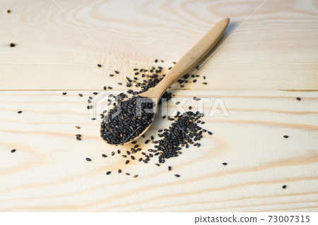 Black sesame seeds in wooden spoon pile on wood table 73007315