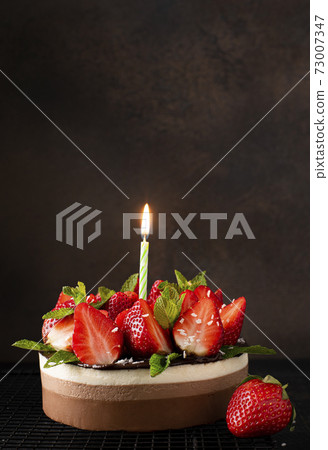 round homemade chocolate cake with fresh strawberries and mint and with burning holiday candle 73007347