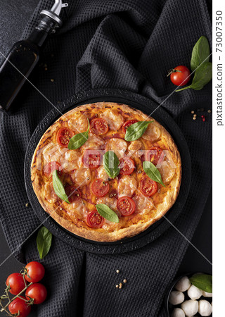 homemade pizza with mozzarella and cherry tomatoes on a black round board 73007350
