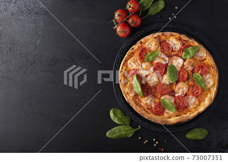 homemade pizza with mozzarella and cherry tomatoes on a black round board homemade pizza with mozzarella and cherry tomatoes on a black round board 73007351