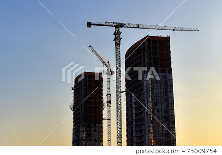 Tower cranes working at construction site on sunset background.  73009754