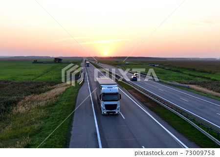 Truck with semi-trailer driving along highway on the sunset background.  73009758