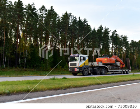 Trailer truck with long platform transport the Excavator on highway. Trailer truck with long platform transport the Excavator on highway. 73009810
