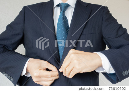 A businessman wearing a suit jacket and buttoning 73010602