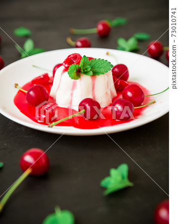Panna cotta with coonut milk, cherry syrup and berries at white plate on a dark background, vegetarian dessert Panna cotta with coonut milk, cherry syrup and berries at white plate on a dark background, vegetarian dessert 73010741