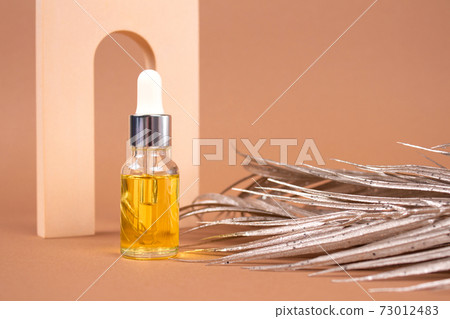 Mockup image of dropper bottle of organic cosmetics - hyaluronic acid, serum, moisturizer or facial anti-aging oil. Essential oil in neutral biege still life composition with golden palm leaves Mockup image of dropper bottle of organic cosmetics - hyaluronic acid, serum, moisturizer or facial anti-aging oil. Essential oil in neutral biege still life composition with golden palm leaves 73012483