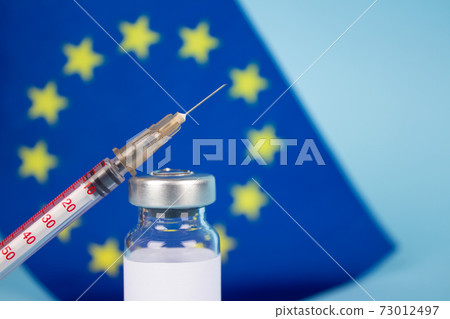 COVID-19 vaccine vial against EU flag on blue background with copy space for text - coronavirus vaccine doses, europe vaccination concept. Selective focus 73012497