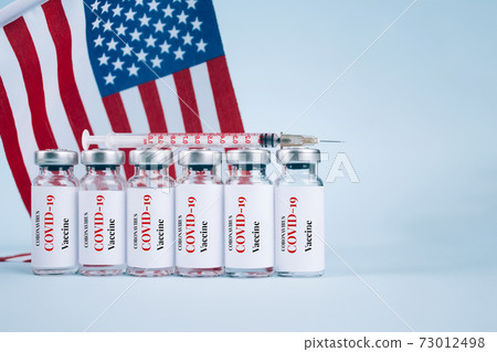 COVID-19 vaccine vials against USA flag on blue background with copy space for text - coronavirus vaccine doses, USA vaccination concept. Selective focus COVID-19 vaccine vials against USA flag on blue background with copy space for text - coronavirus vaccine doses, USA vaccination concept. Selective focus 73012498