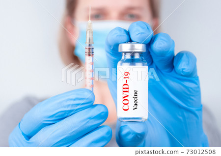 Female doctor or woman scientist wearing medical face mask and holding COVID-19 vaccine - protection against coronavirus, global vaccination concept. Selective focus Female doctor or woman scientist wearing medical face mask and holding COVID-19 vaccine - protection against coronavirus, global vaccination concept. Selective focus 73012508