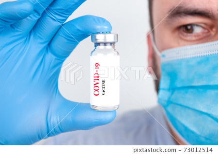 Doctor or scientist wearing medical face mask and holding COVID-19 vaccine - protection against coronavirus, global vaccination concept. Selective focus Doctor or scientist wearing medical face mask and holding COVID-19 vaccine - protection against coronavirus, global vaccination concept. Selective focus 73012514