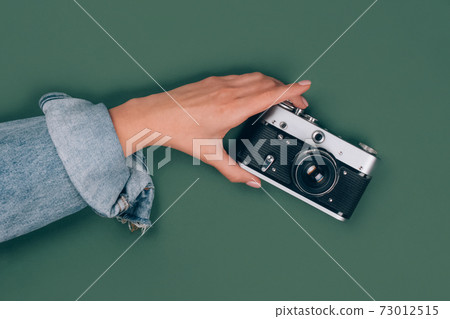 Closeup view of female hand holding old retro photo camera on green background with copy space for text. Trendy vintage photography, online photography school concept. Selective focus Closeup view of female hand holding old retro photo camera on green background with copy space for text. Trendy vintage photography, online photography school concept. Selective focus 73012515