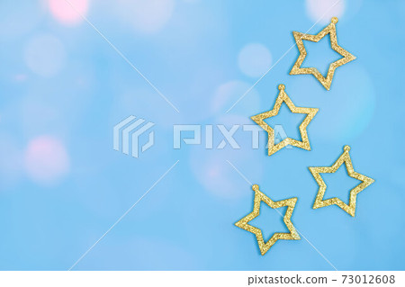 Golden Christmas ornaments - stars decorations on pastel blue background with copyspace. Festive and New Year celebration concept. Selective focus Golden Christmas ornaments - stars decorations on pastel blue background with copyspace. Festive and New Year celebration concept. Selective focus 73012608