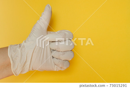 A hand in a white latex glove gives a thumbs up sign on a yellow background A hand in a white latex glove gives a thumbs up sign on a yellow background 73015291