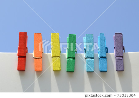 Seven wooden multi-colored clothespins, painted in the colors of the rainbow, against the blue sky 73015304