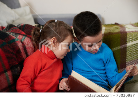 Two children, a little boy and girl sitting close to each other looking at a family photo album. Brother and sister Two children, a little boy and girl sitting close to each other looking at a family photo album. Brother and sister 73020987