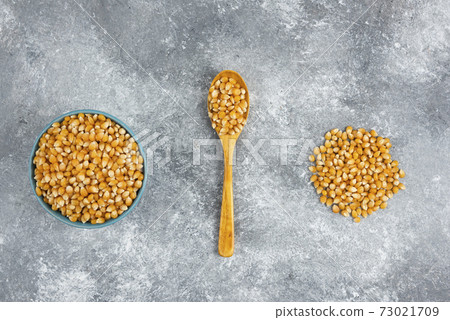 Uncooked corn kernels in blue bowl on marble surface 73021709