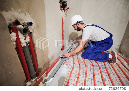 Male worker installing underfloor heating system in apartment. Male worker installing underfloor heating system in apartment. 73024708