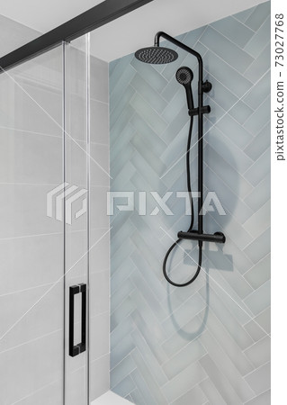 Modern shower zone with rain head, hand held shower and glass door. Light blue and white tiles in the bathroom Modern shower zone with rain head, hand held shower and glass door. Light blue and white tiles in the bathroom 73027768