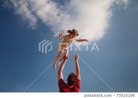 little girl 3 years flies out of daddy's hands against blue sky 73028106
