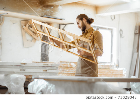Carpenter with window frame at the workshop Carpenter with window frame at the workshop 73029045