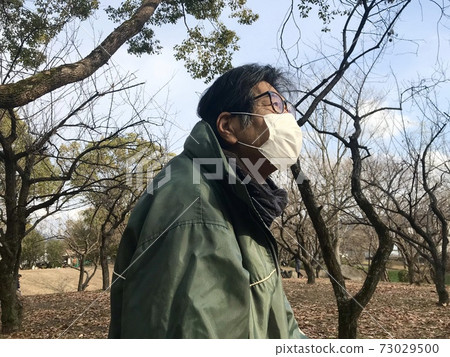 A man in his 60s wearing a mask and taking a walk in the park on a cold day 73029500