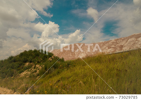 Soligork salt mine slagheap mountains and scenic beautiful nature with green grass and dramatic cloudy sky in hot summer day 73029785