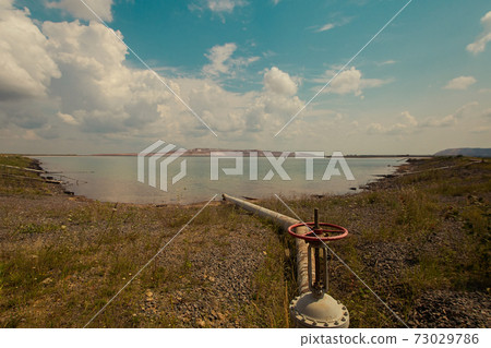 Soligork salt mine scenic nature with green grass and dramatic cloudy sky in summer day. A technical water lake, industrial metal constructions, brine pipeline, old rusty pipes and tap Soligork salt mine scenic nature with green grass and dramatic cloudy sky in summer day. A technical water lake, industrial metal constructions, brine pipeline, old rusty pipes and tap 73029786