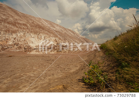 Soligork salt mine slagheap mountains and scenic nature with green grass and dramatic cloudy sky in summer day. A technical water lake and white salt rock 73029788