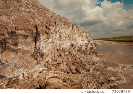 Soligork salt mine slagheap mountains and scenic nature with green grass and dramatic cloudy sky in summer day. A technical water lake and white salt rock 73029789