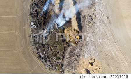 Excavators clear the field from the forest to increase farmland. Burning trees in a pit after increasing the plowed field. Inefficient farming. The burning of the forest. Environmental problem. 73031906